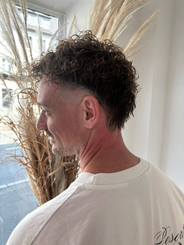 7197ccf8 3a89 4081 a209 1a69567b3475 Wir lieben Haare Mann mit lockigem Mullet und kurzem Fade-Schnitt im Profil